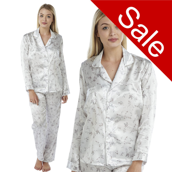 ivory background with a purple floral and hummingbird print silky shiny satin pjs set consisting of a shirt style top with full length sleeves, a collar, top pocket and a button up front with matching full length trousers in UK sizes 8, 10, 12, 14